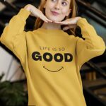 Bright yellow oversized sweatshirt with the phrase 'Life Is So Good' and a minimalistic smiley face.